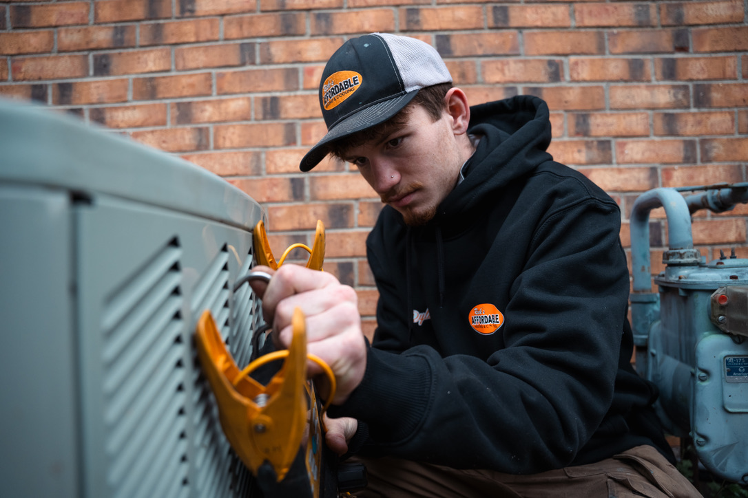 HVAC service technician taking amperage readings on an outdoor AC condenser in Toledo, Ohio