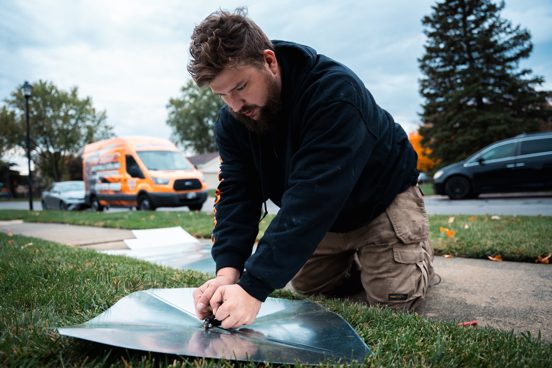 Rick's Affordable Heating & Cooling installer fabricating sheet metal ductwork beside a company service van
