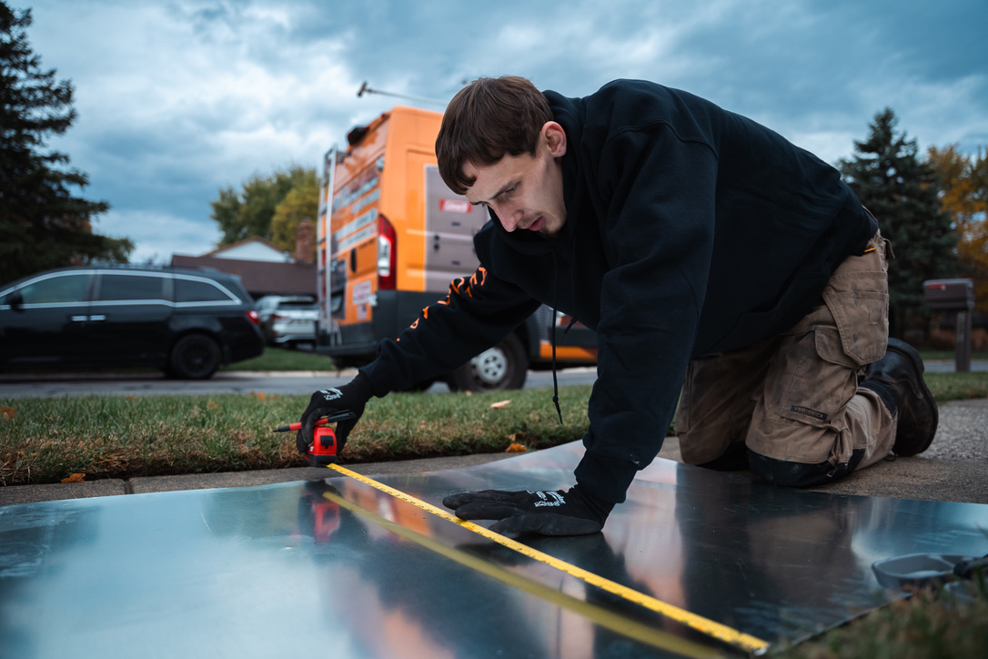 Install helper measuring sheet metal for a furnace duct transition on a Perrysburg job site