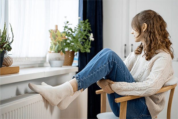 Woman warming feet on heater after heating service in Perrysburg, OH by Rick's Affordable Heating and Cooling