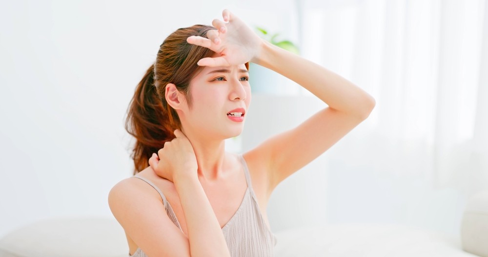 An overheated woman putting her hand to her head.