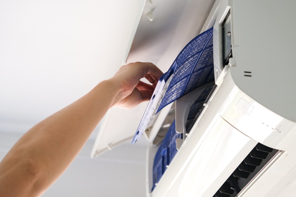 A technician removing a filter from a mini split air conditioning unit for cleaning