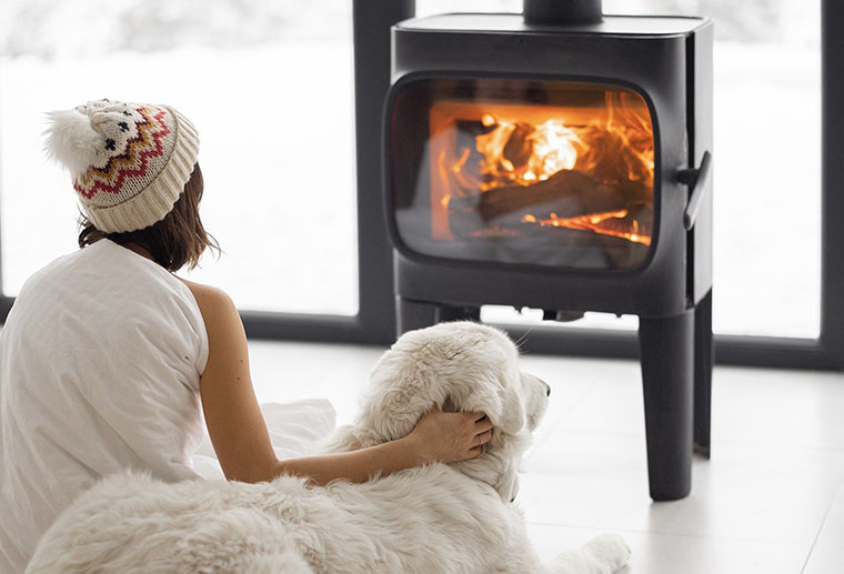 Woman sitting cozy with dog by fireplace installed by Ricks Affordable Heating and Cooling in Perrysburg, Ohio