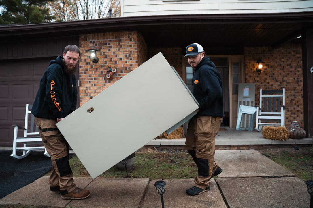 Two Rick's Affordable technicians carrying a new furnace unit at a customer's front door