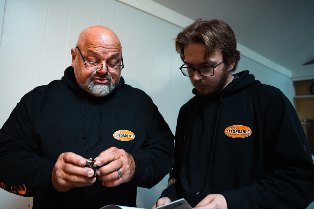 Rick's Affordable senior and junior technician inspecting an HVAC component together