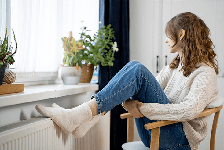 Woman warming feet on heater after heating service in Perrysburg, OH by Ricks Affordable Heating and Cooling